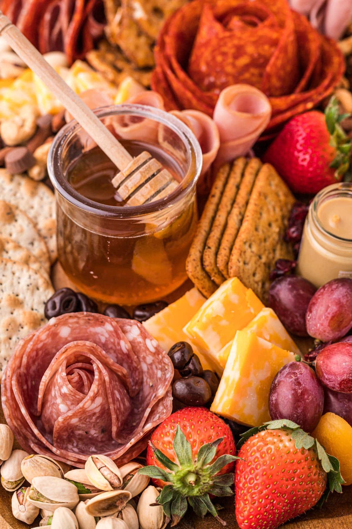 close up of charcuterie board with small jar of honey, crackers, cheese, fruit, and meats