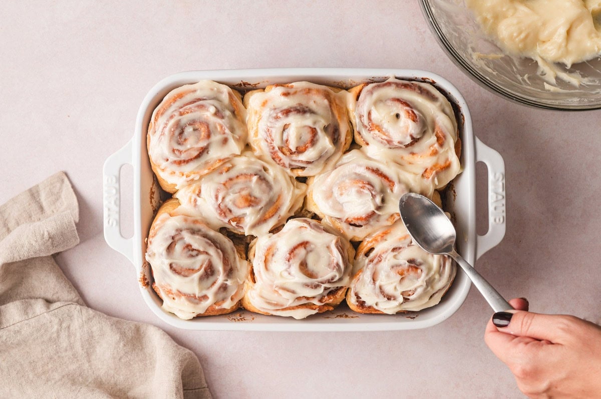 cinnamon rolls with icing and a spoon spreading the icing.