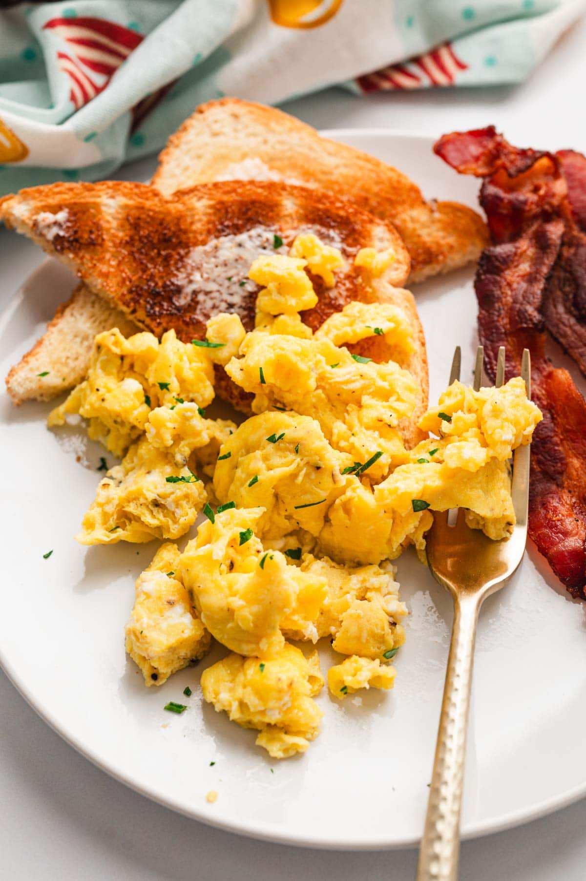 Scrambled egg, bacon and toast on a white plate.