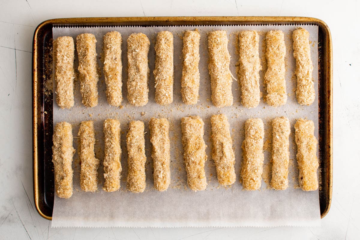 Breadcrumb coated mozzarella cheese sticks on a baking sheet.