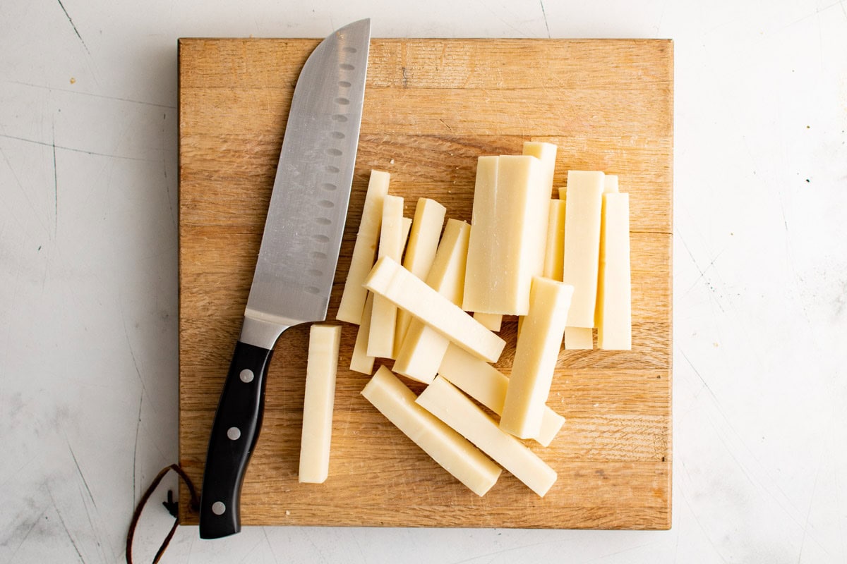 Sticks of mozzarella cheese on a cutting board with a knife.