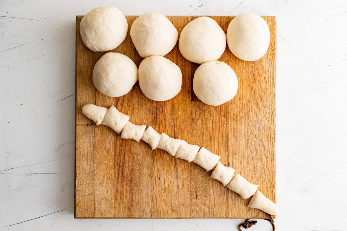 Balls of bread dough and a long rope of dough cut into small pieces.