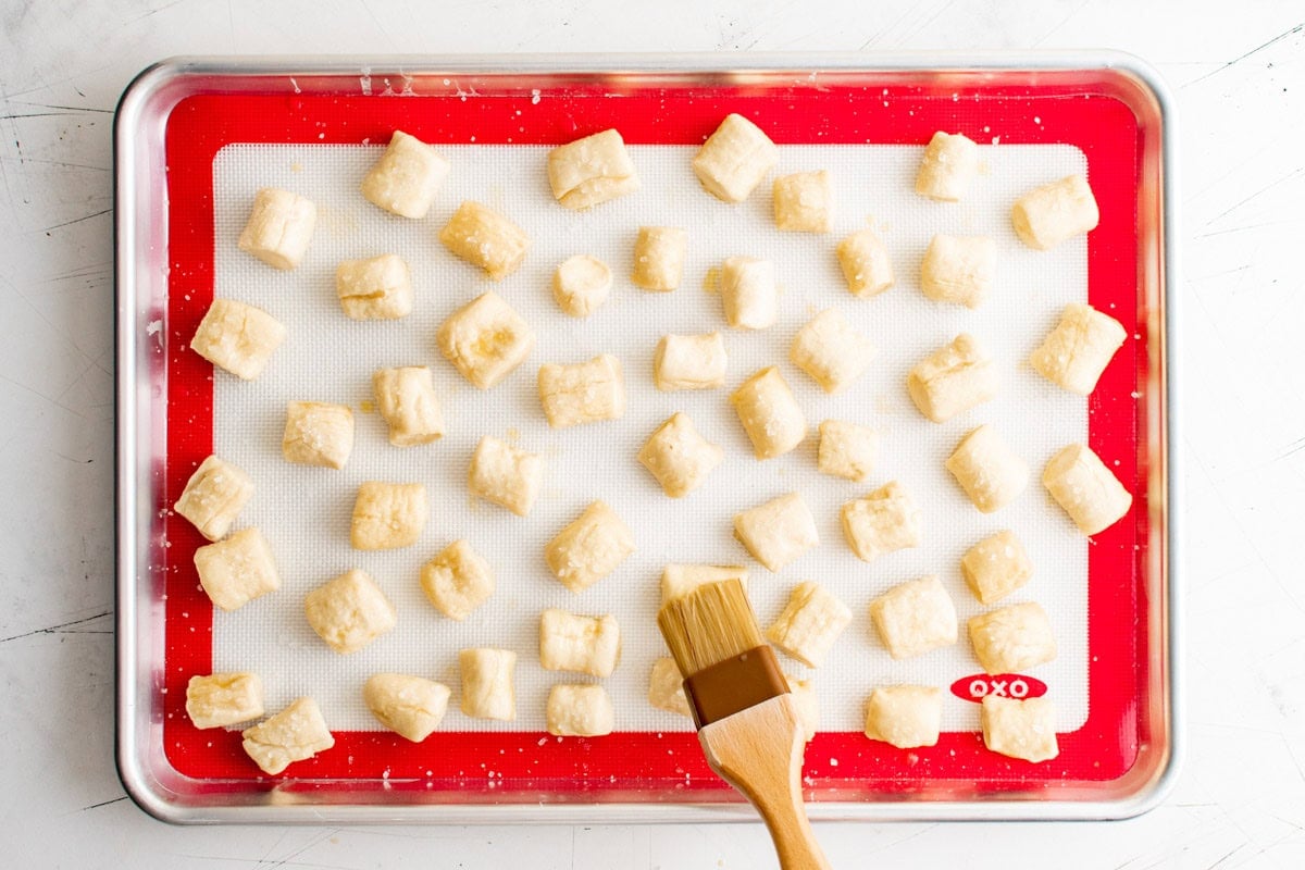 Pretzel bites on a baking sheet being brushed with egg wash.