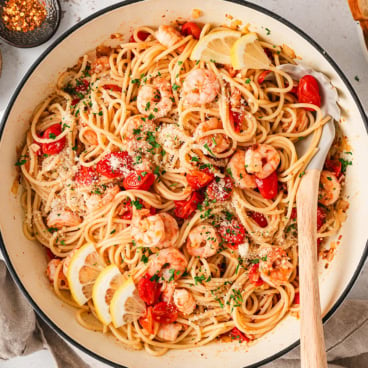 Shrimp and spaghetti in a pan iwth a wooden spoon.