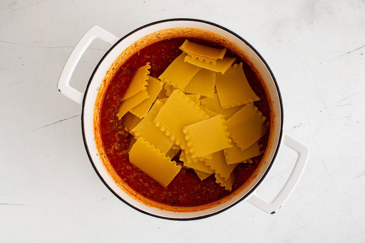 Broken lasagna noodles sitting on top of marinara sauce in a large pot.