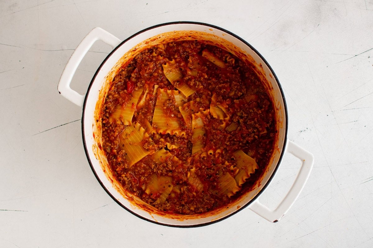 Red sauce mixed with lasagna noodles in a large pot.