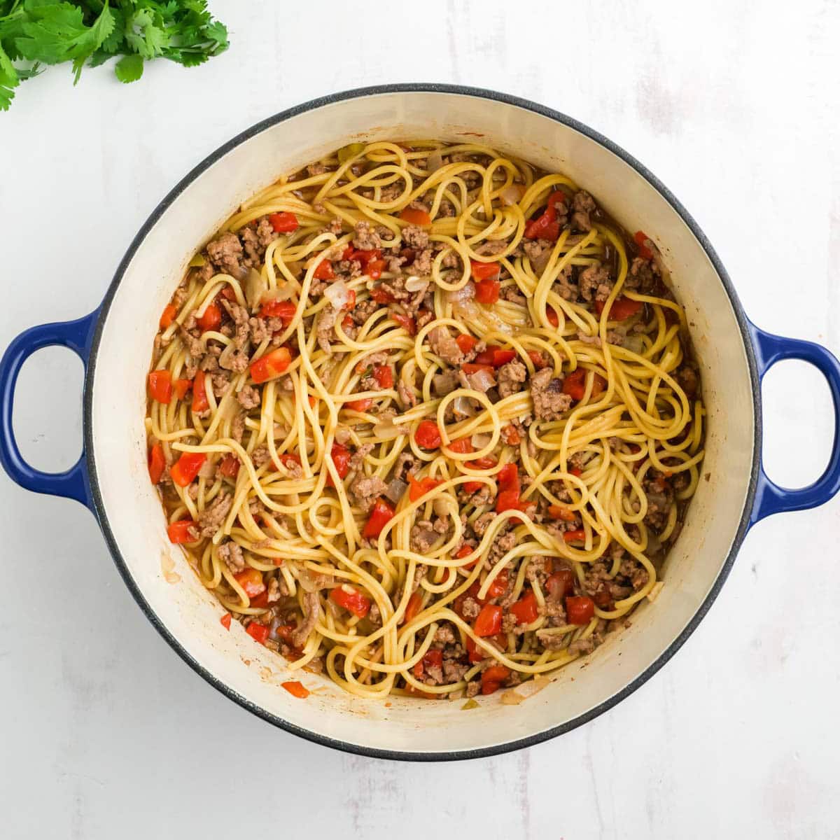 Cooked spaghetti, ground beef and diced tomatoes in a pot.