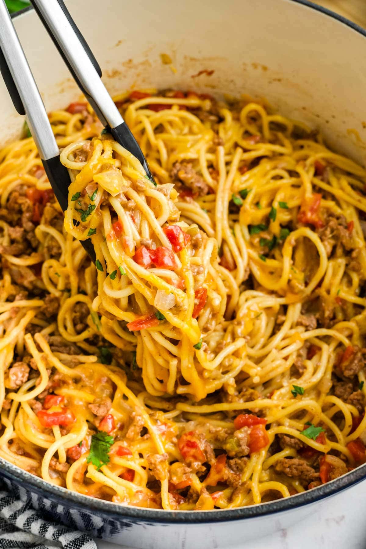 Metal tongs lifting spaghetti with ground beef and tomatoes.