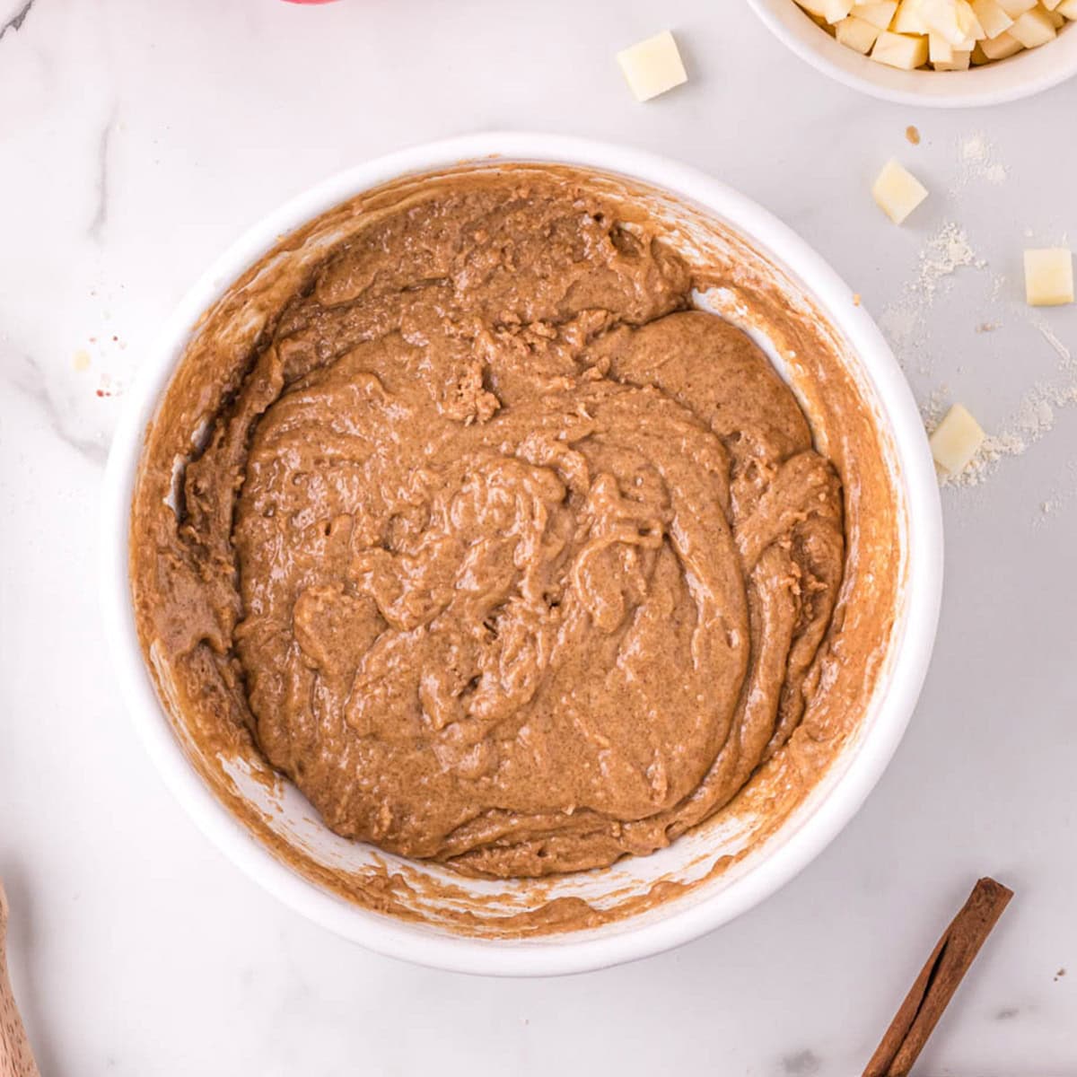 Brown batter for cinnamon apple muffins in a white mixing bowl.