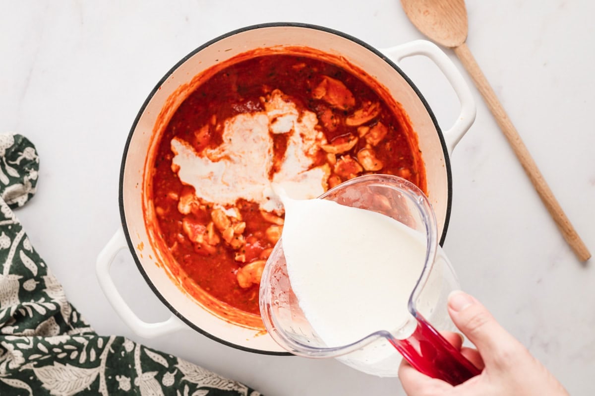 tomato sauce and chicken with cream pouring from a measuring cup.
