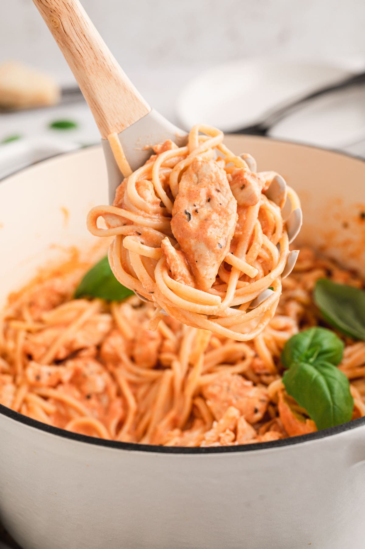 Linguine with chicken in a creamy tomato sauce in a pan with fresh basil leaves