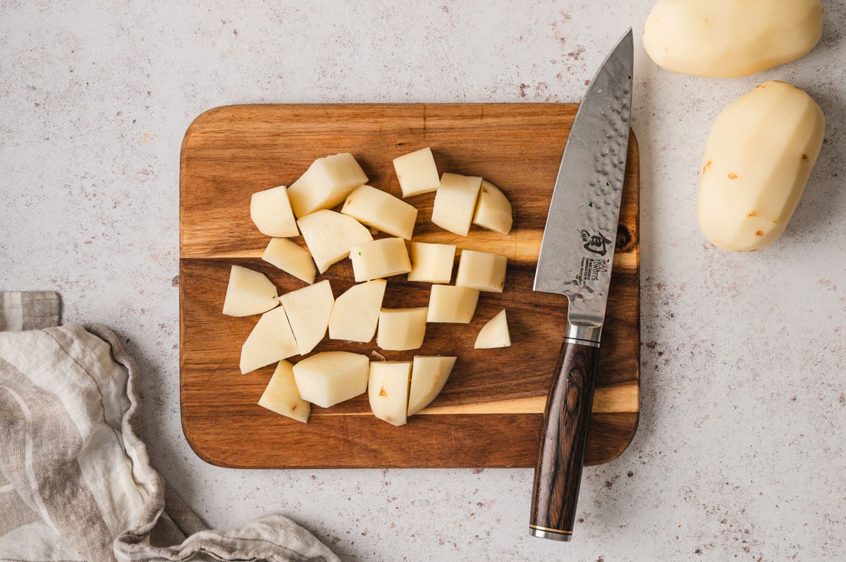 Chunks of potatoes on a cutting board with a knife.