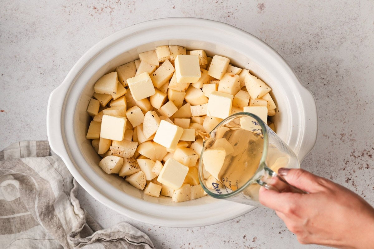 chunks of potato in a slow cooker pot with a measureing cup.