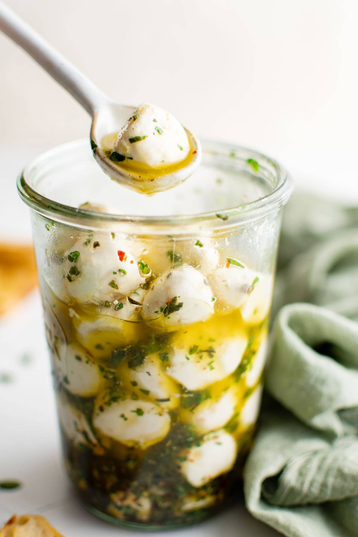 Marinated mozzarella balls in a jar with a white spoon.