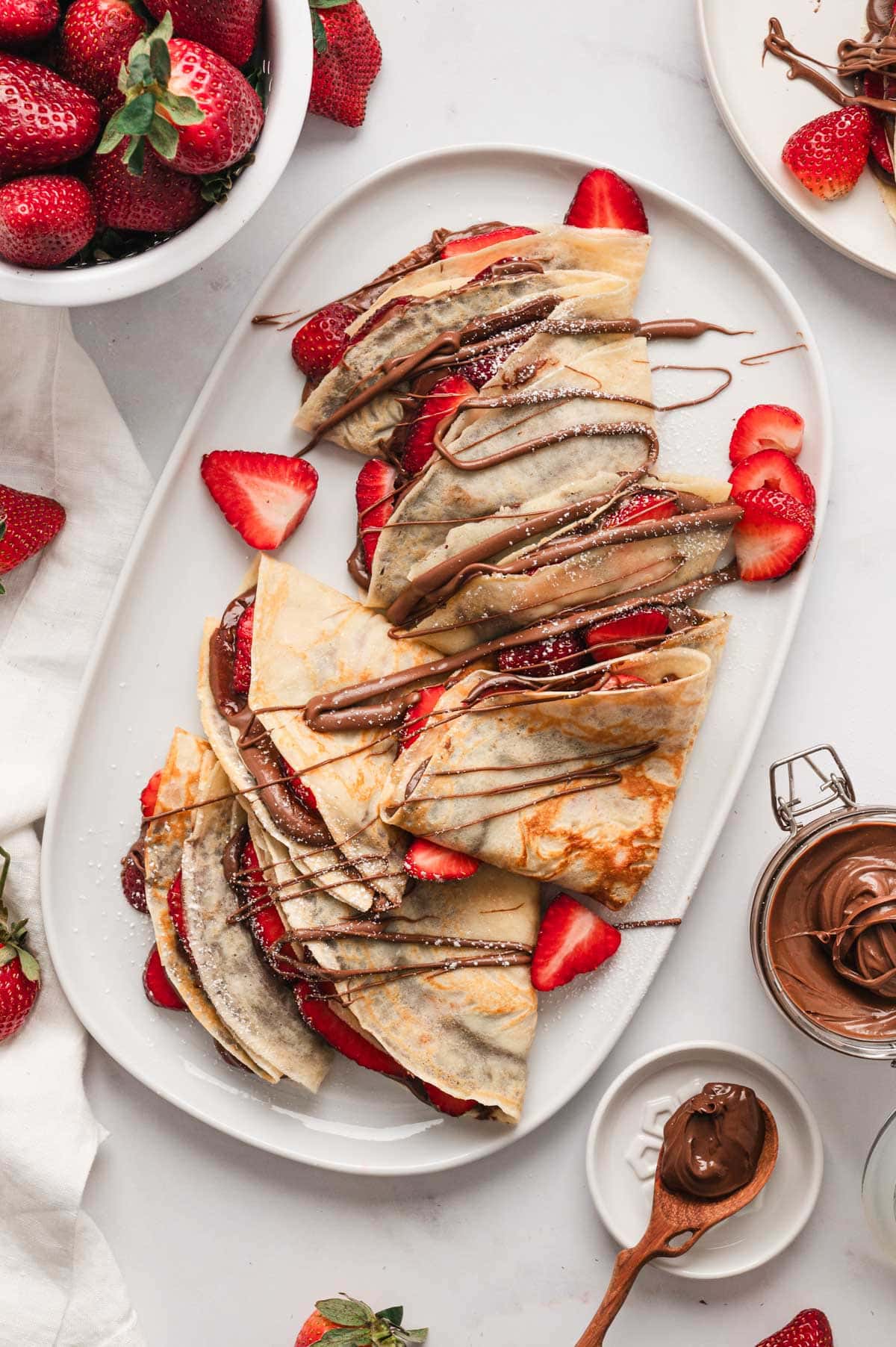 Crepes with chocolate and strawberries on a white platter. 