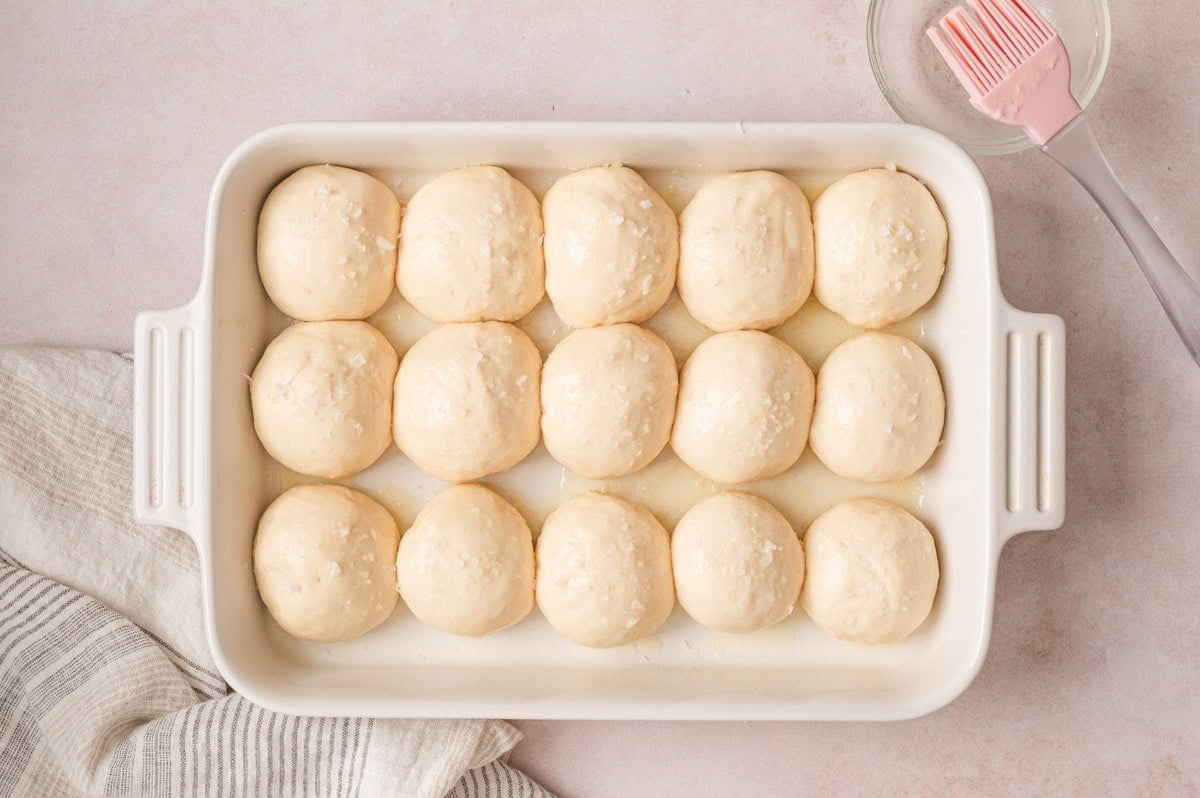 Portion dinner rolls rising in a baking dish.