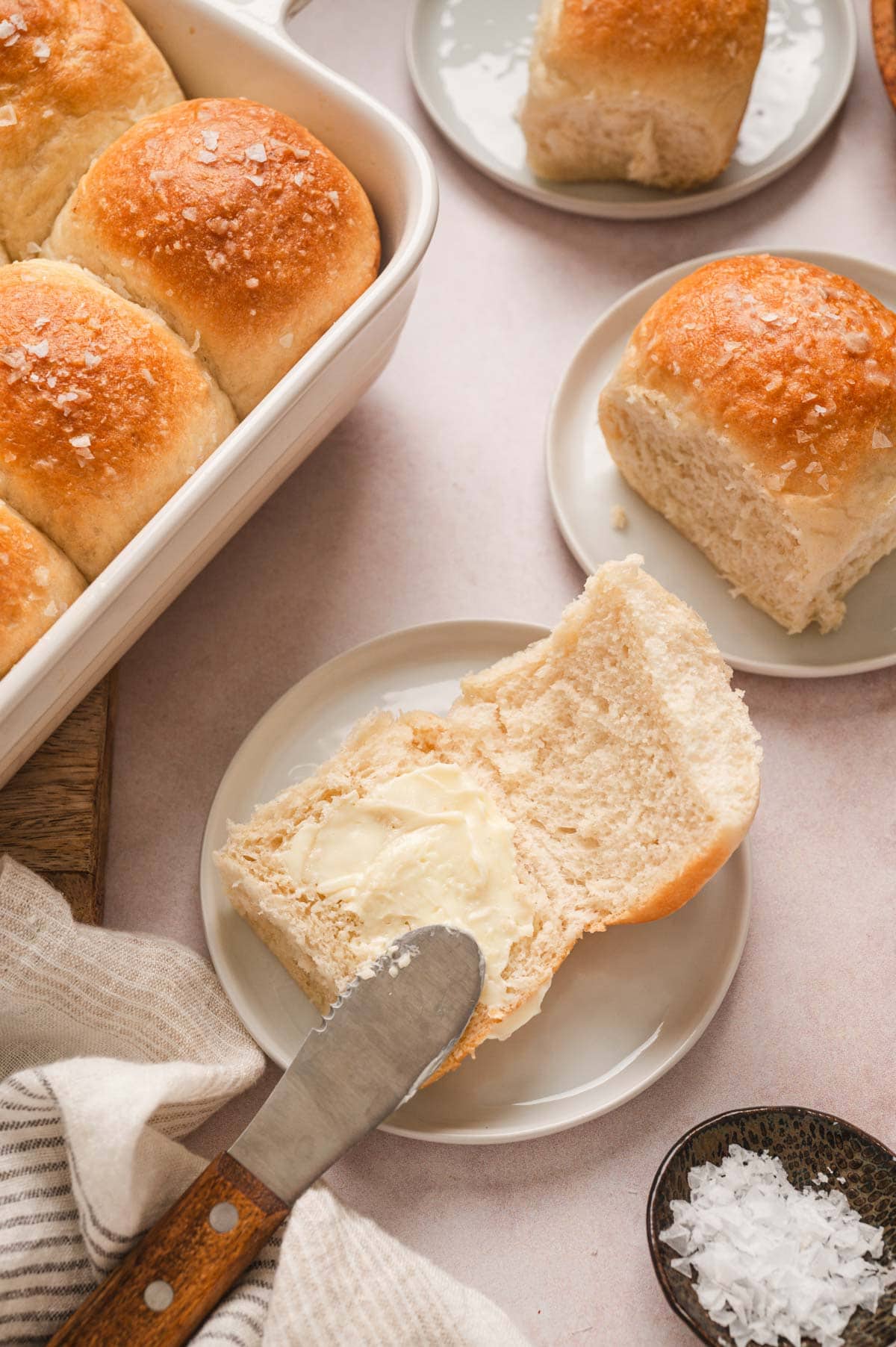 dinner roll split in half with a knife spreading butter.