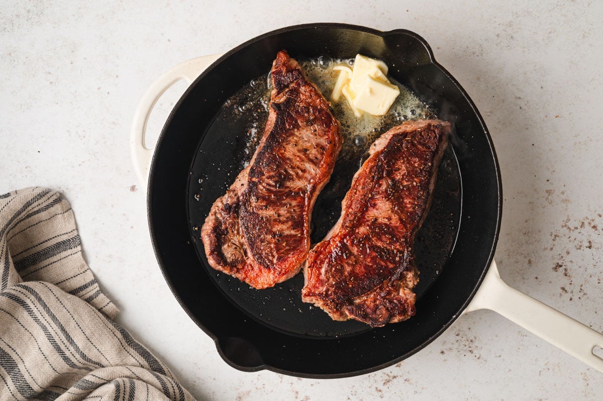 cast iron pan with 2 steaks and melting butter