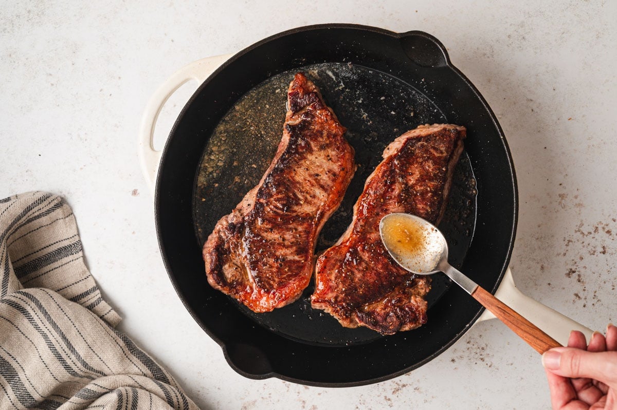 Spooning juices oven steaks in a skillet
