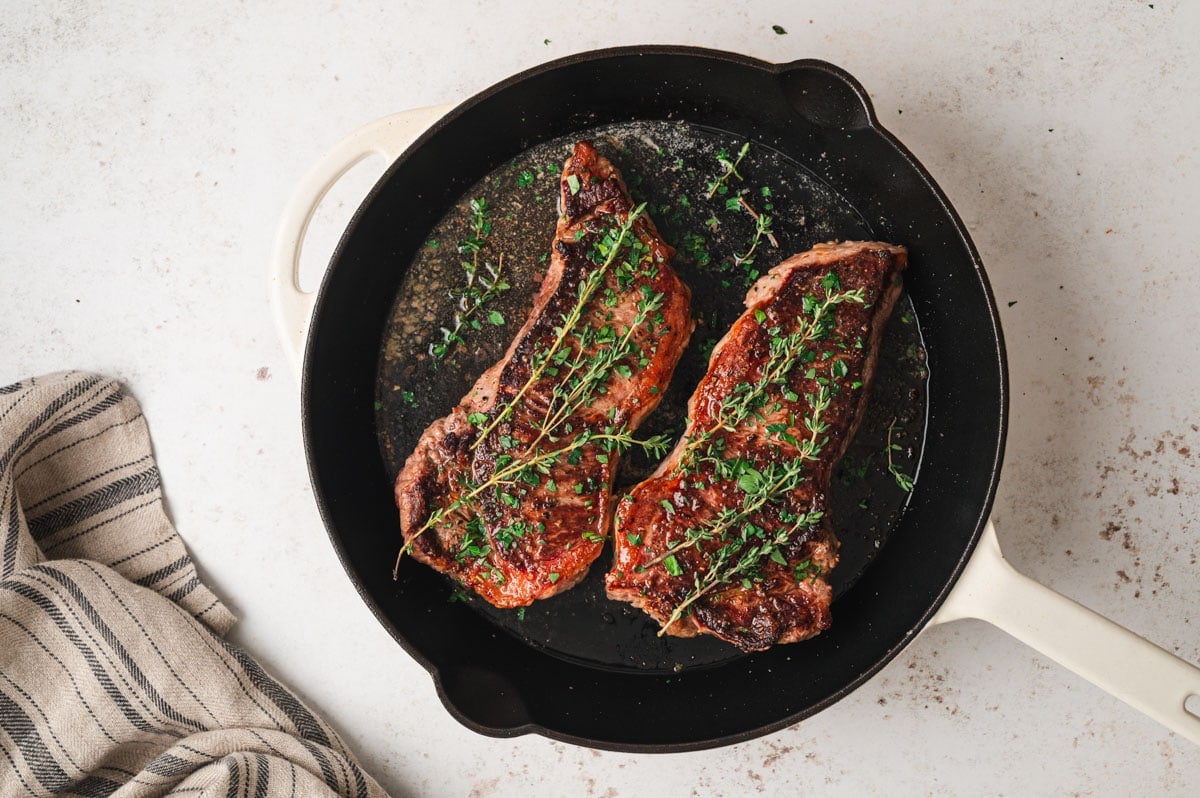 Seared steaks in a skillet with springs of thyme