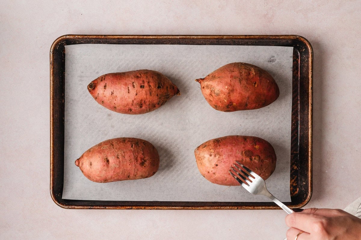 Sweet potaotes on a sheet pan poked with a fork.