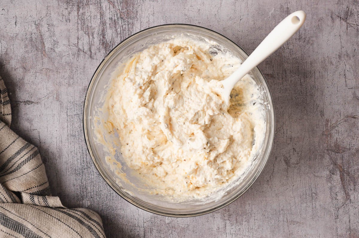 Ricotta cheese mixture in a glass bowl with a spatula.