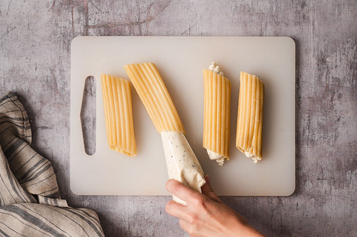 Piping cheese filling into manicotti shells.