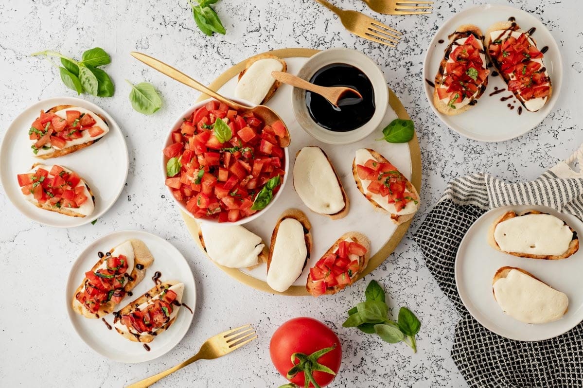 Different ways to serve mozzarella bruschetta, in bowls and on platters with gold utensils. 